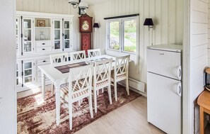 A kitchen with white cabinetry, a dining table with chairs, a clock, and a refrigerator.