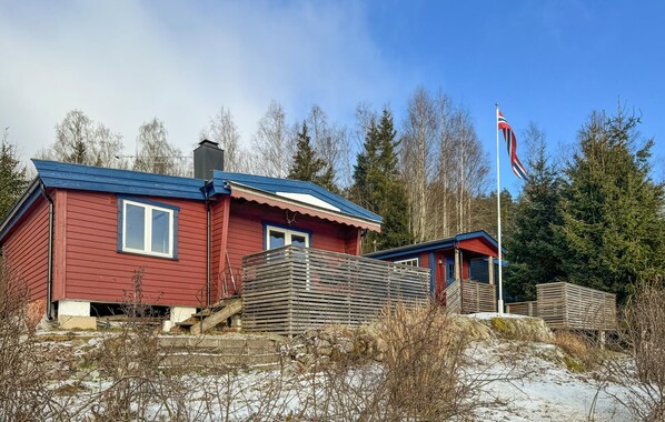 A red wooden house with a blue roof, a flagpole with a flag, and a forested background.