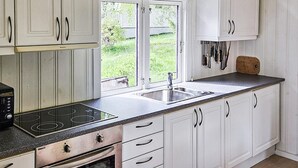 Een keuken met witte kasten, een dubbele spoelbak, een fornuis en een raam met uitzicht op groen.