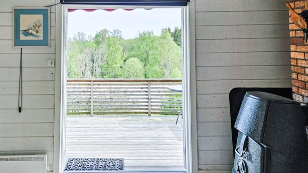 Een kamer met een houten vloer, een deur naar een terras, een zwarte stoel en een lijst met een afbeelding aan de muur.