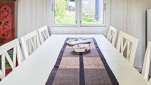 Een eettafel met witte stoelen, een geweven placemat en twee witte borden met fruitmotieven.