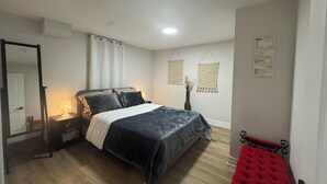 Ein Schlafzimmer mit Bett, Nachttisch, Lampe und einem roten Sessel.