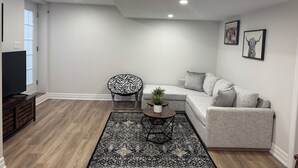 Ein modernes Wohnzimmer mit einem grauen Sofa, einem schwarz-weißen Stuhl, einem kleinen runden Tisch mit einer Pflanze und einem schwarz-weißen Teppich.