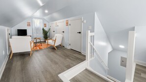 Una habitación amplia con techo alto, sofá blanco, una mesita y una silla. Hay puertas que dan a otras habitaciones y una escalera.