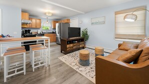 Una cocina moderna con armarios de madera, un refrigerador de acero inoxidable y una zona de comedor con taburetes blancos.