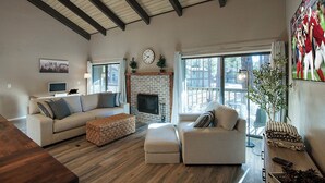 A spacious living room with a fireplace, two sofas, a coffee table, and a large window providing a view of the outdoors.