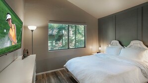A bedroom with a bed, a TV on a dresser, a window with a view of trees, and a lamp.