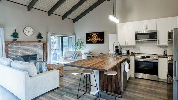 A modern kitchen with white cabinets, stainless steel appliances, and a wooden island with stools.