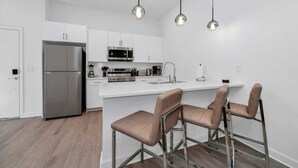 Een moderne keuken met witte kasten, roestvrijstalen apparatuur en een centraal eiland met barkrukken.