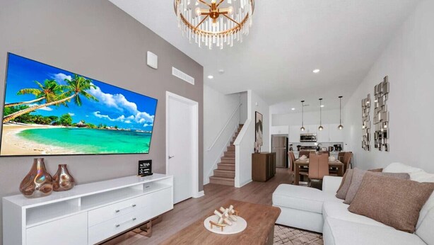 Een moderne woonkamer met een flatscreen-televisie, witte banken, een houten salontafel en een trap die naar een keuken leidt.