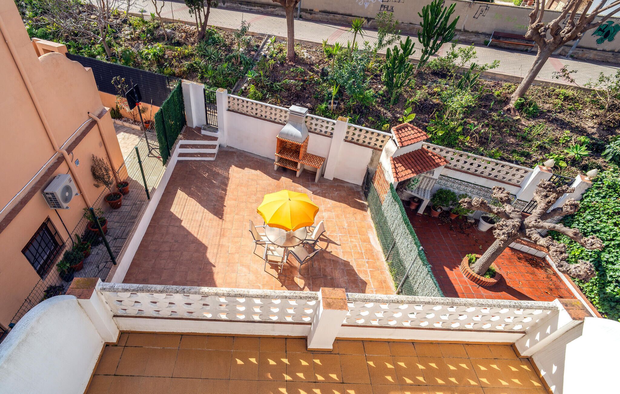 Una terraza en la azotea con una sombrilla amarilla, mobiliario de exterior y plantas en macetas.