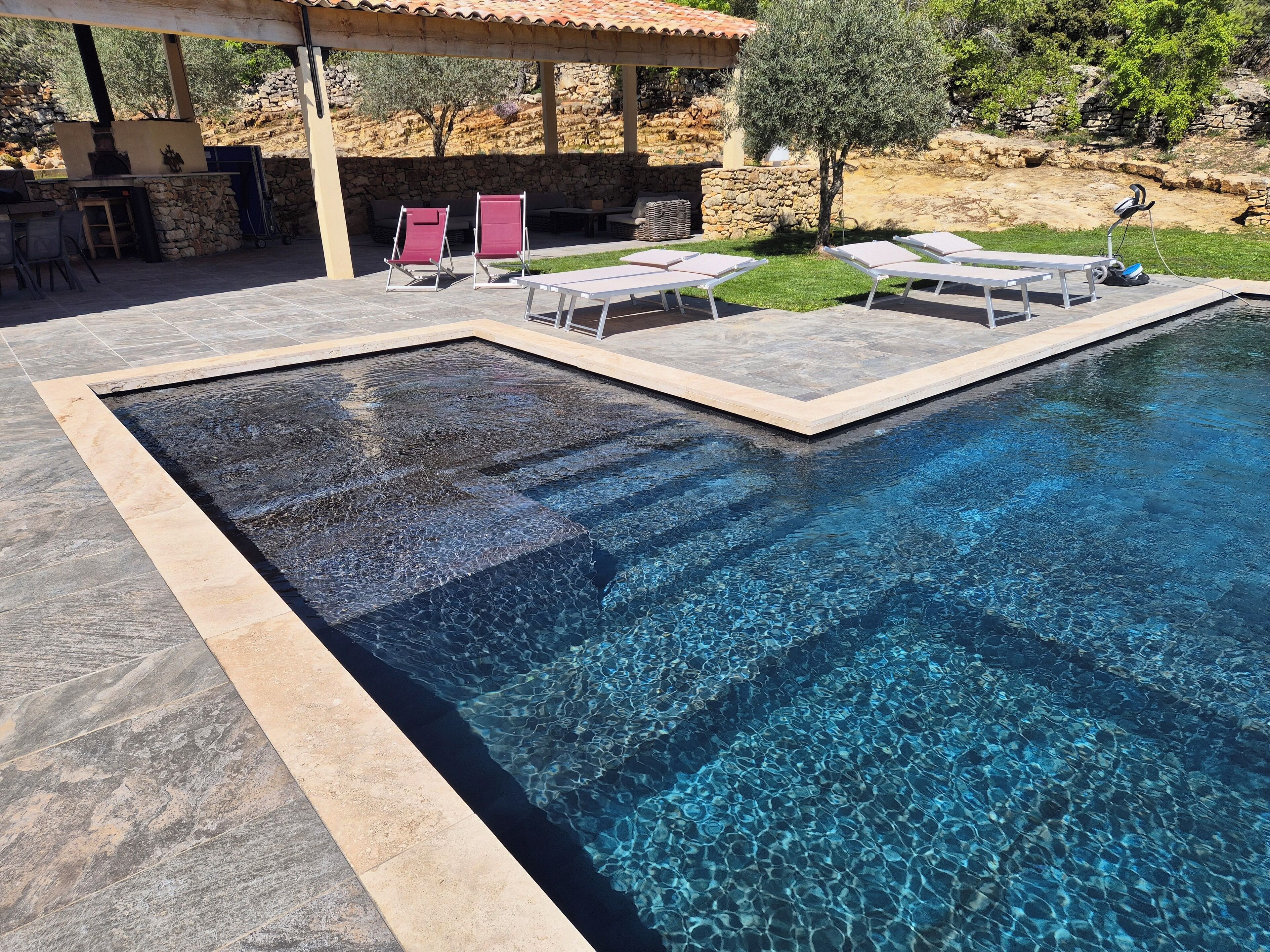 Una piscina d'aigua cristal·lina, envoltada de gandules i una zona de terrassa de pedra.