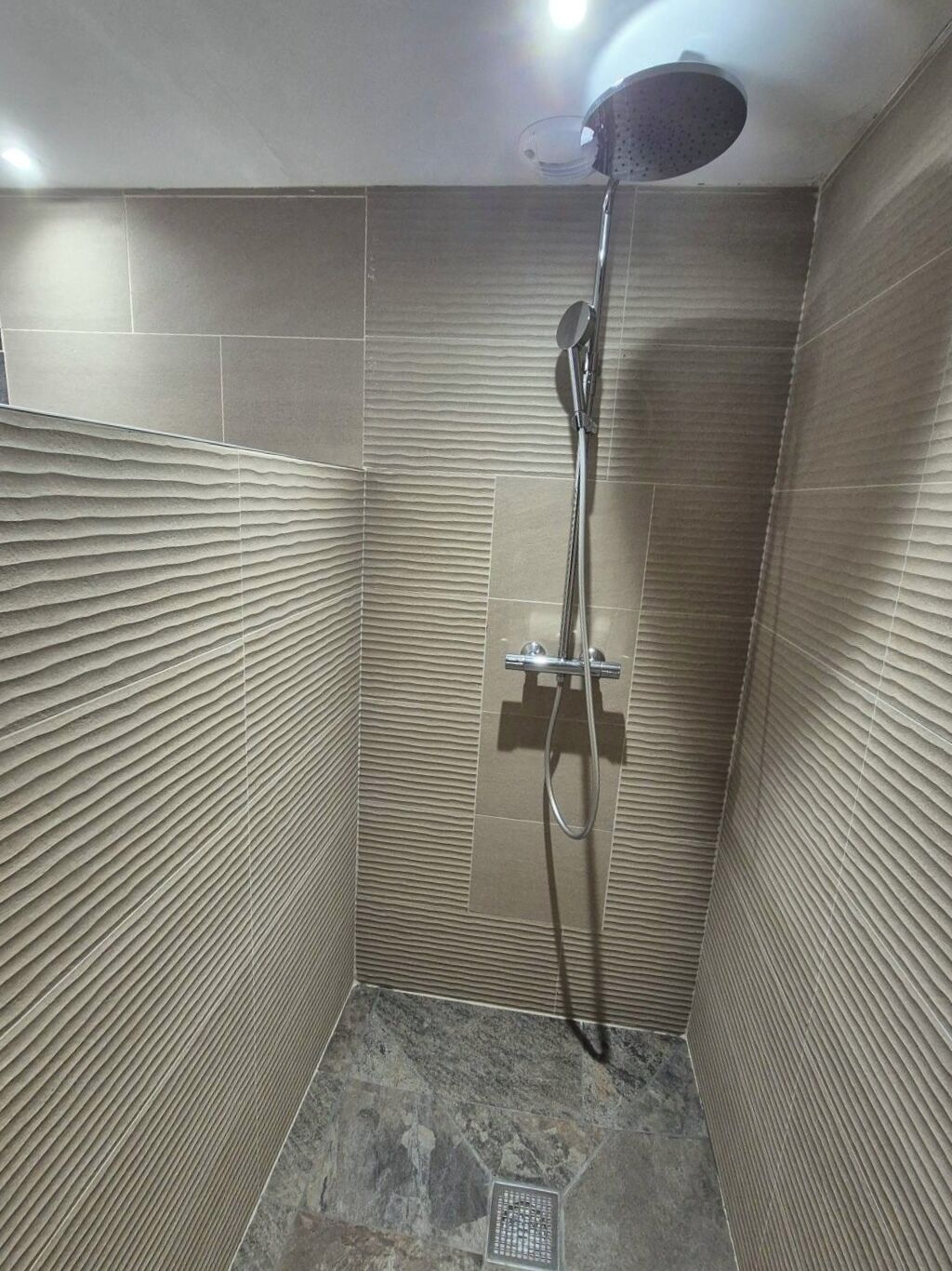 Un piccolo bagno rivestito di piastrelle con doccetta a mano e rubinetto montato a parete.