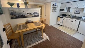 Une cuisine compacte avec des meubles blancs, un four à micro-ondes et un panneau indiquant la présence d’une connexion Wi-Fi. Un coin repas avec une table et des chaises en bois est situé à côté de la cuisine.