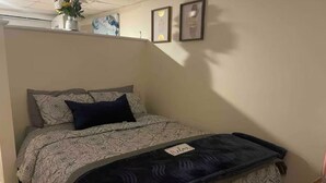 Une chambre à coucher comprenant un lit, une table de chevet et une étagère murale ornée d’un vase et de tableaux encadrés.
