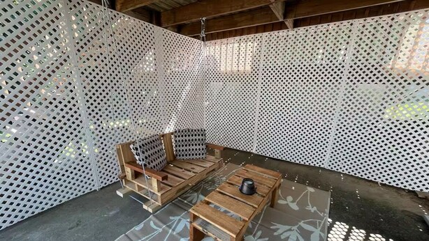 Une pièce avec un banc en bois, une petite table et une cloison blanche perforée.