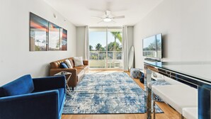 Un salon moderne avec un canapé, des fauteuils bleus, une table basse et un téléviseur.