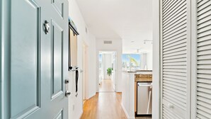 Un couloir avec un coin cuisine, doté d’un plancher en bois, de murs blancs et d’une porte avec une poignée.