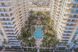 Un hôtel de grande hauteur doté de nombreux balcons, d’une piscine centrale entourée de palmiers et d’une cour intérieure.