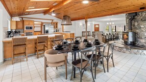 A spacious kitchen with wooden cabinets and a large island, a dining area with a round table and chairs, and a stone fireplace in the background.
