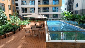 Un área de piscina en la azotea con cubierta de madera, sillones de descanso y barandilla de cristal.