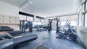 Un gimnasio con diversos equipos de ejercicio, un espejo grande y amplias ventanas.