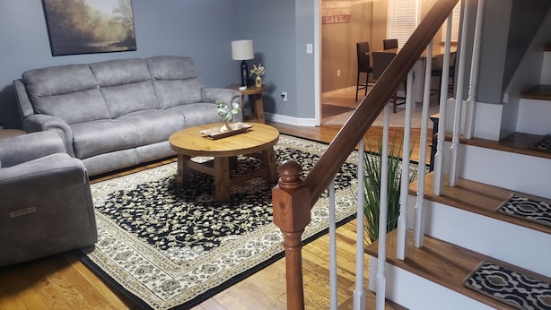 A living room with a grey sofa, a round wooden coffee table, and a patterned rug.
