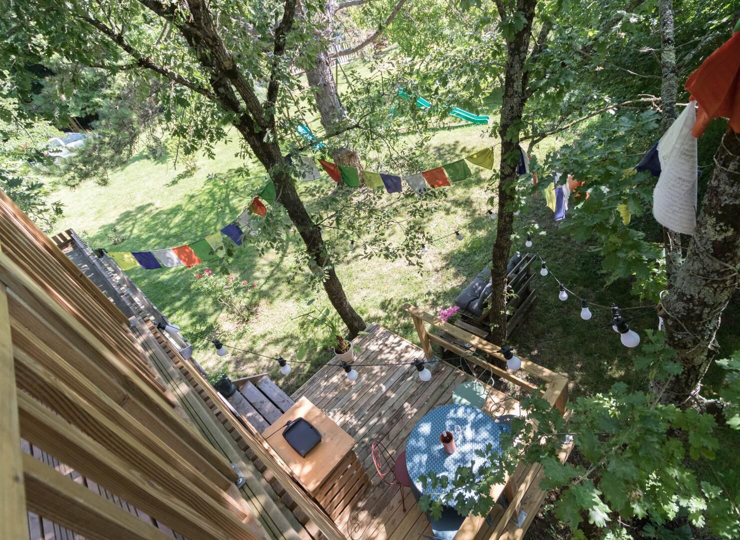 A wooden deck with a table and chairs, surrounded by trees and a grassy area.