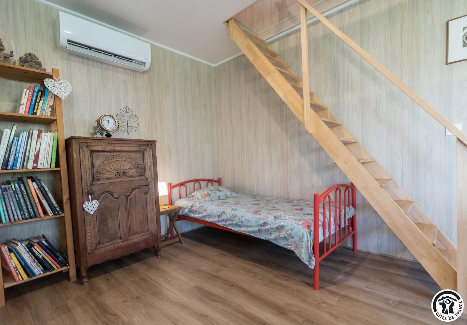 Ein Schlafzimmer mit einem Holzbett, einem Nachttisch mit Büchern und einer Wandklimaanlage.