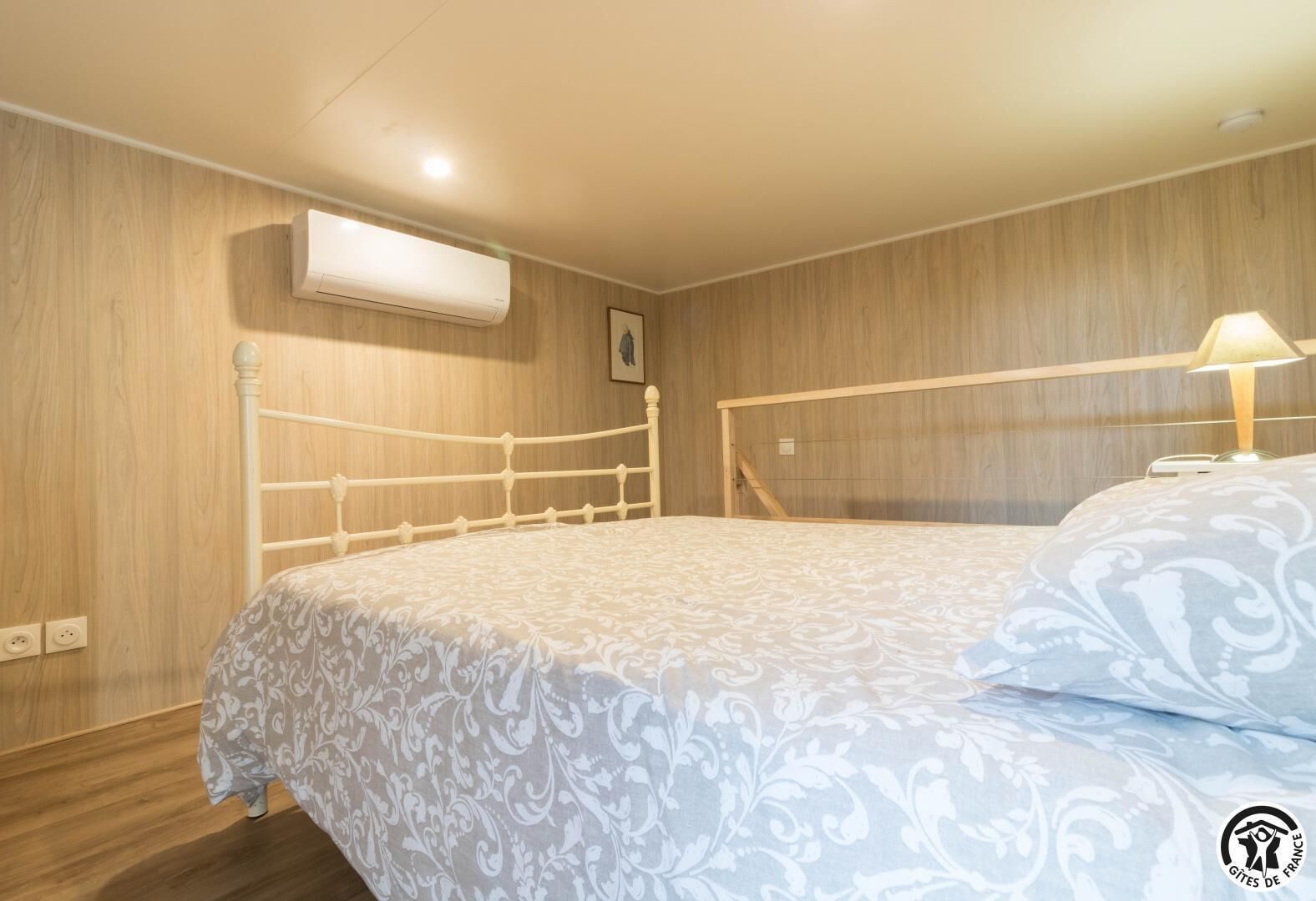 Una camera da letto con testiera in legno, un letto con copriletto decorato, un condizionatore d'aria e un comodino con lampada.