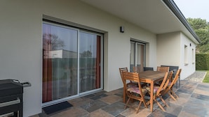 Une terrasse avec une table et des chaises en bois, un barbecue et une porte-fenêtre coulissante.