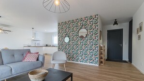 Un salon moderne avec un canapé gris, un miroir rond et un mur orné d’un motif.