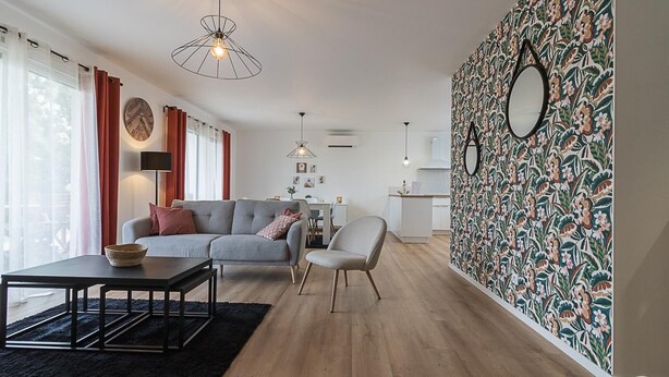 Un salon moderne avec un canapé gris, une table basse noire et un mur orné d’un motif.