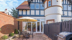 Un patio con una griglia, mobili da esterno e vista su una casa in stile Tudor.
