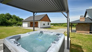 Un jacuzzi bajo una zona techada, con una casa y un edificio de ladrillo al fondo.