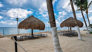A beach with thatched umbrellas, lounge chairs, and a sandy walkway.