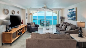 A living room with a TV, sofas, a wooden cabinet, and a dining area with a view of the ocean.