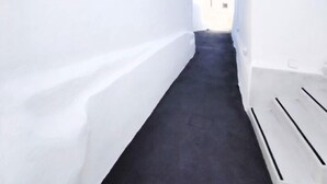 A narrow corridor with white walls and a dark floor, leading to a door. - Nolis White Fira (Santorini)