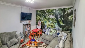 Un salon comprenant un canapé, une petite table, une bibliothèque et une fresque représentant une forêt.