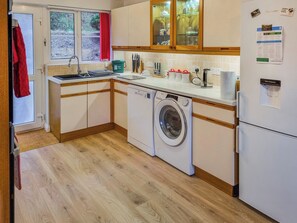 A compact kitchen with wooden cabinets, a washing machine, a sink, and a refrigerator.