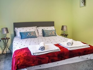 A neatly made bed with a red blanket, two pillows with floral designs, and two folded towels on the bed.