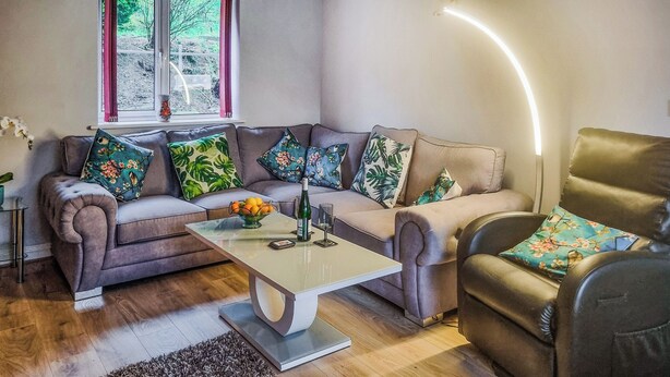Un salon avec un canapé, une table basse et un fauteuil. Il y a une fenêtre avec des rideaux, un tapis et une plante.