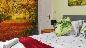Une chambre à coucher ornée d’une grande fresque murale aux motifs automnaux, avec un lit recouvert d’une literie blanche et agrémenté d’oreillers à motifs de feuilles vertes, un plaid rouge et une porte blanche.