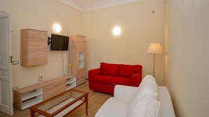 A living room with a red sofa, white sofa, TV mounted on a wooden cabinet, and a floor lamp. - Awesome home in Siracusa with WiFi (Siracusa)