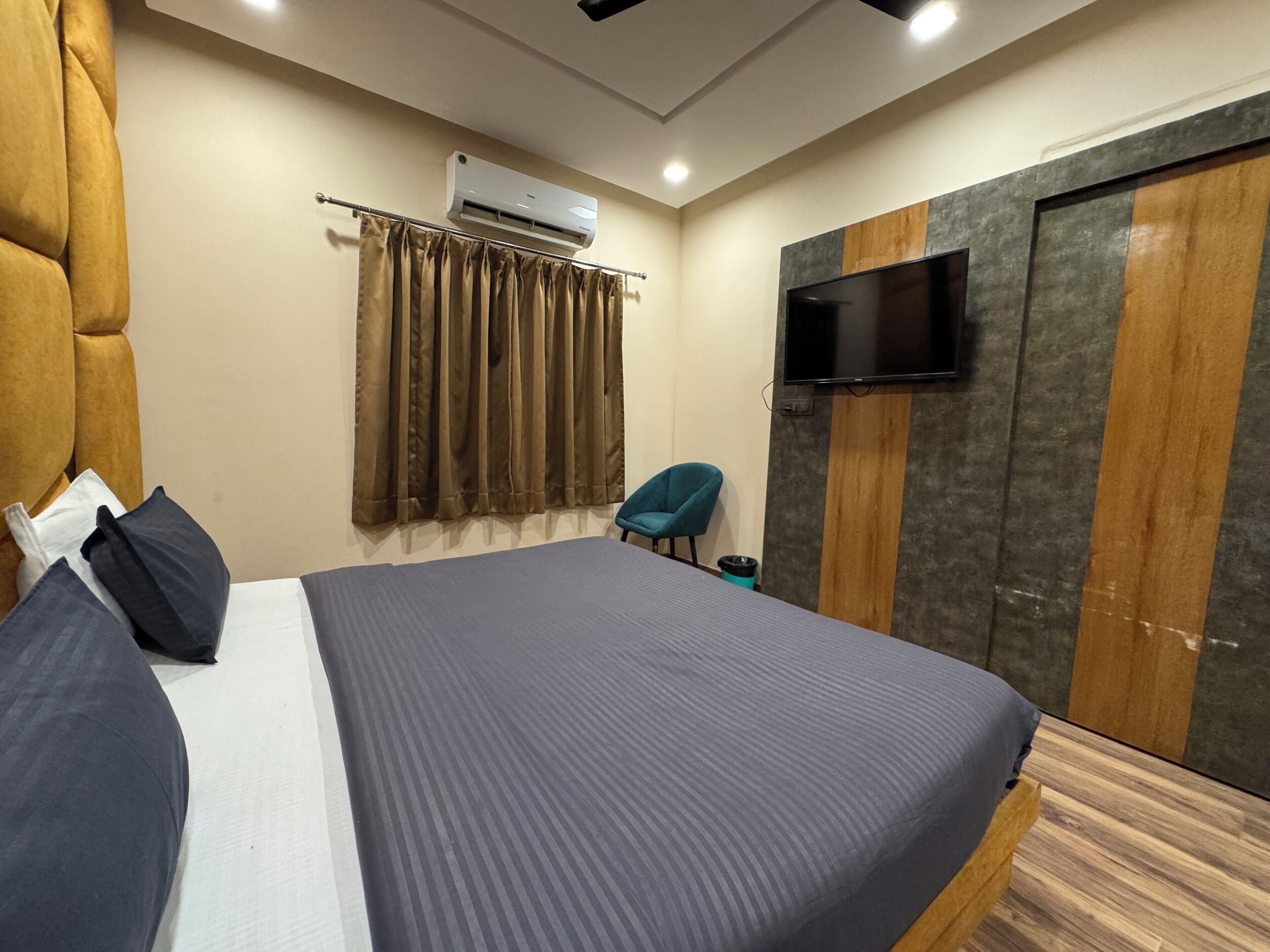 A bedroom with a large bed, a flat-screen TV mounted on a wooden panel wall, and an air conditioning unit on the ceiling.