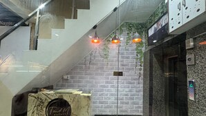 Zona de recepción de un hotel con mostrador de mármol, una escalera y lámparas colgantes.