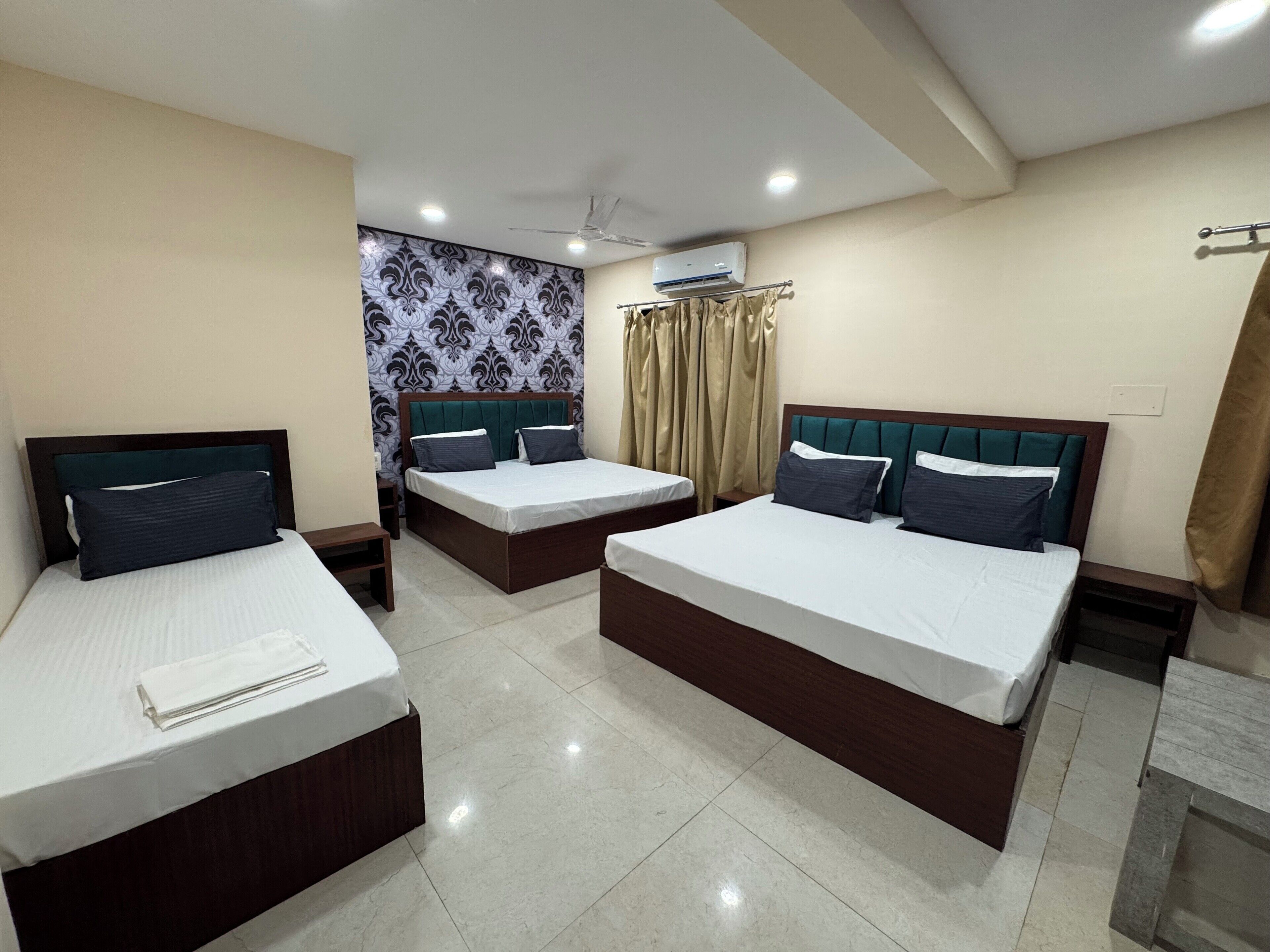 Quarto de hotel com duas camas de solteiro, ventilador de teto, aparelho de ar condicionado e papel de parede estampado.