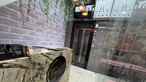 Zona de recepción de un hotel con un mostrador de mármol, un televisor montado en la pared y un panel de vidrio con mantel a cuadros.