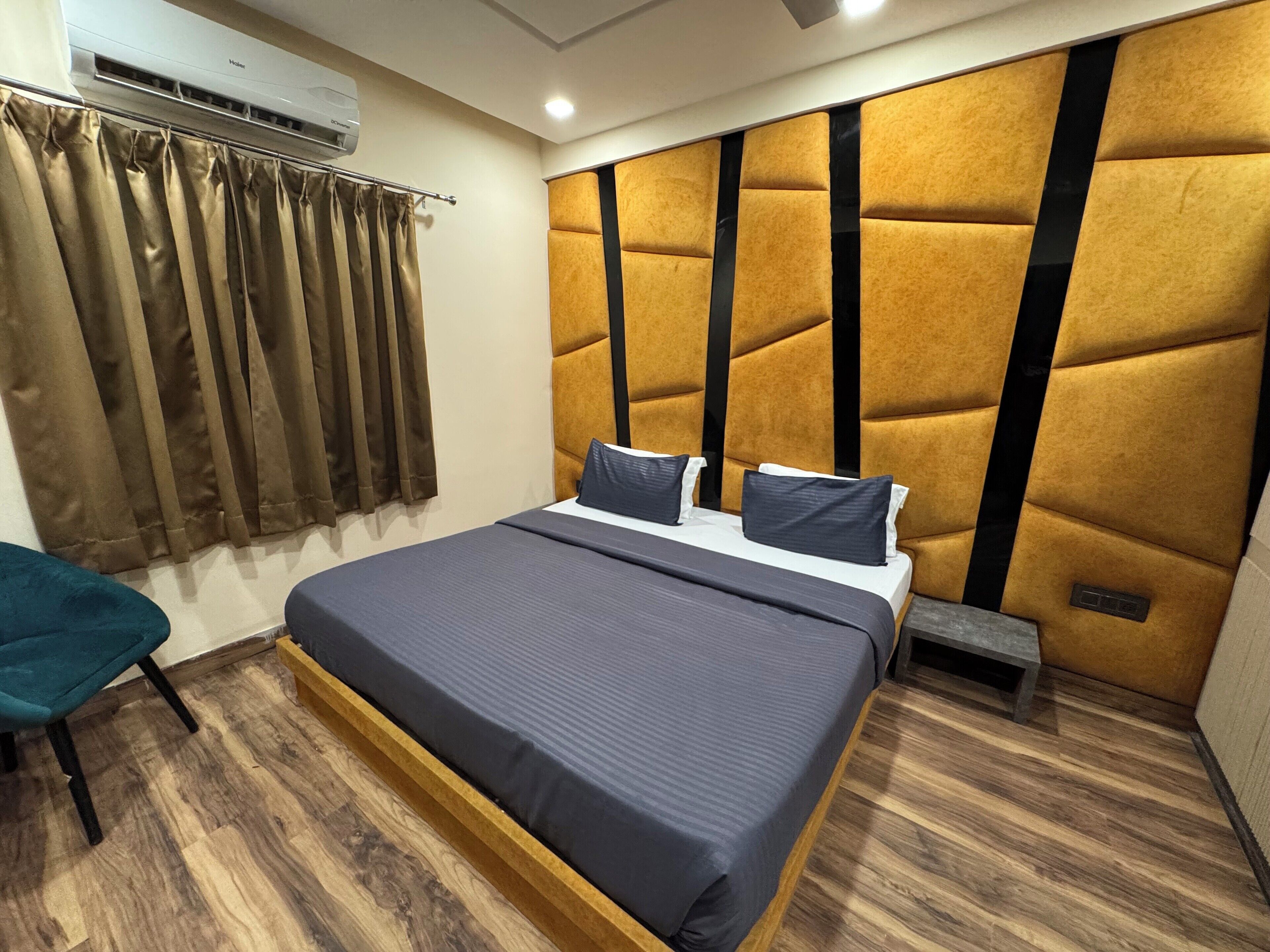 A modern bedroom with a large bed, a wooden floor, a headboard with a geometric pattern, and a window with curtains.