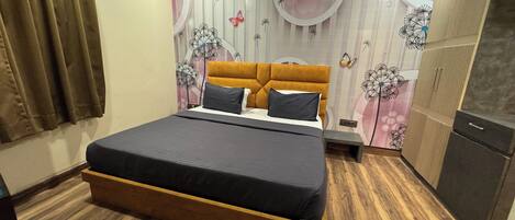 A bedroom with a bed, wooden floor, curtains, a wardrobe, and a wall with floral and dandelion patterns.